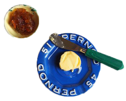 blue plate with foreign writing around the rim adorned with a pad of softened butter paired with a butter knife with a green handle. Pale yellow bowl of jelly sits beside it.