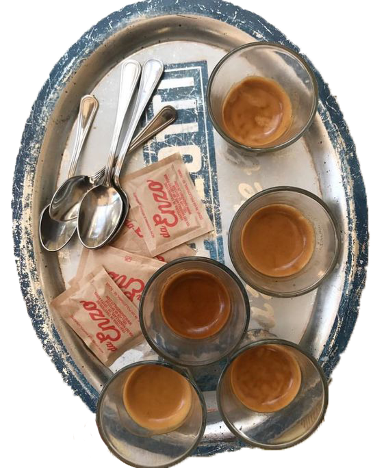 collection glasses with a small amount of coffee at the bottom, silver spoons, and empty sugar packets on a weathered, metal bus tray